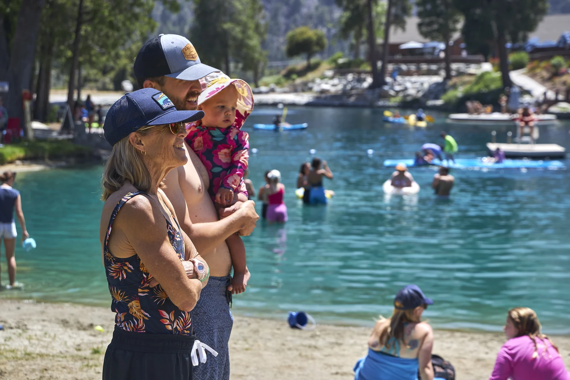 family camp couple holding toddler lakeside swimmers background