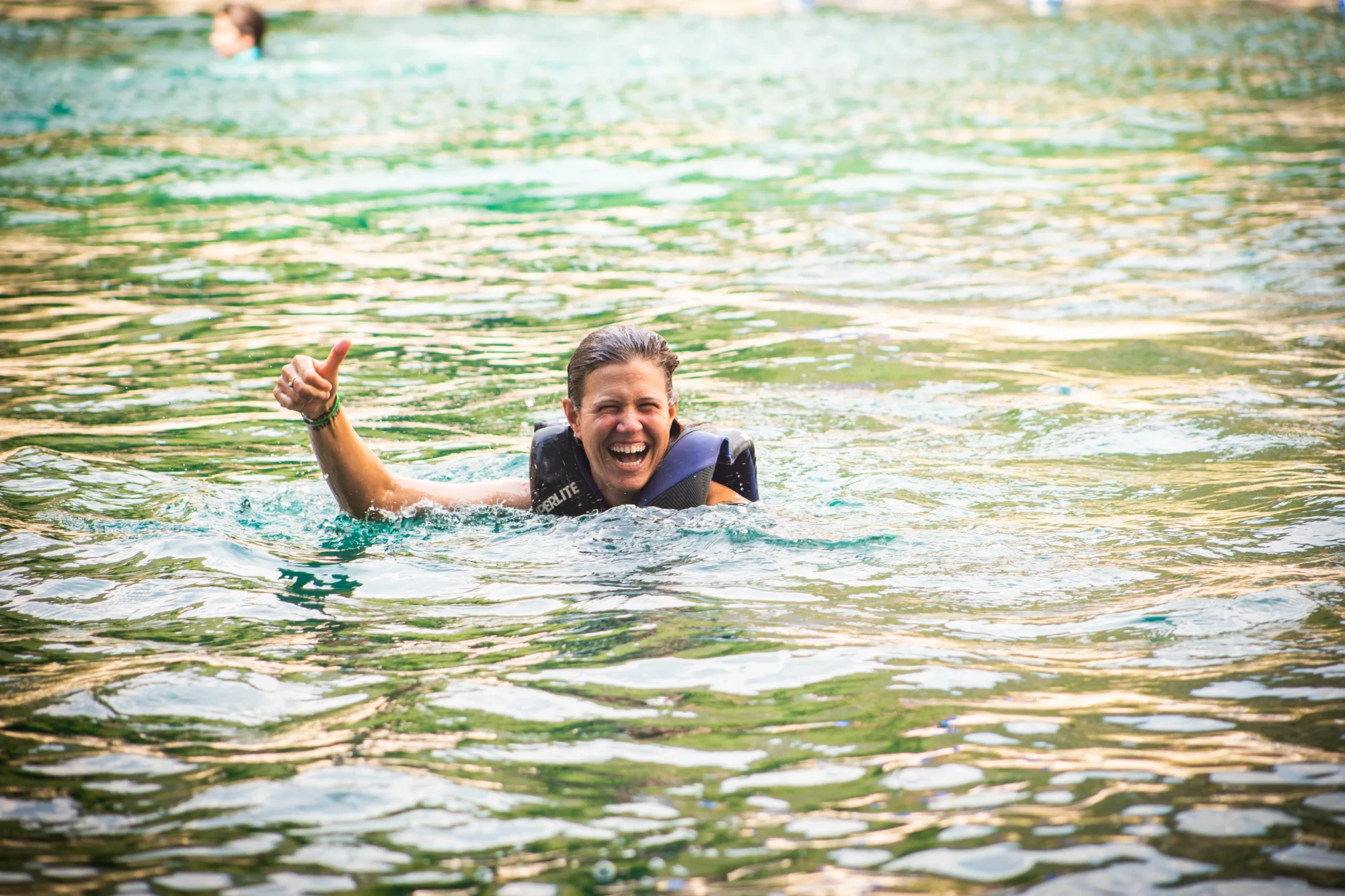 family camp woman in life vest swimming thumbs up in lake